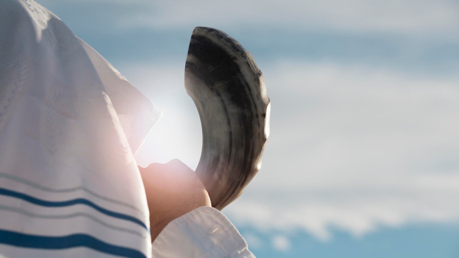 Jewish man blowing the Shofar against blue sky